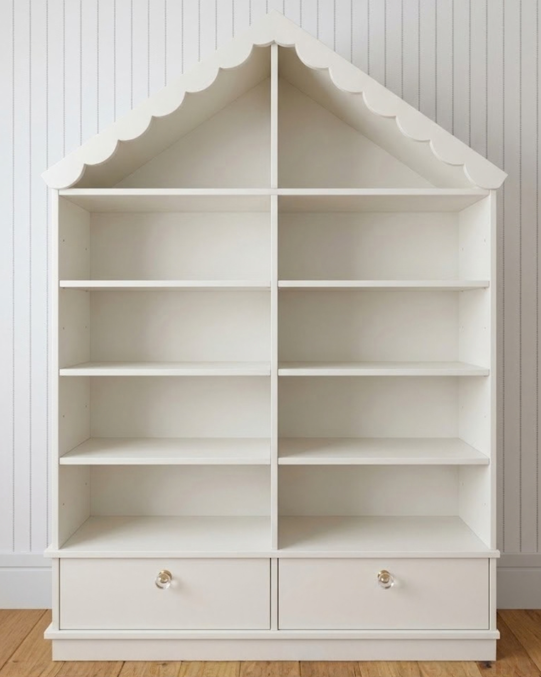 Estante Fábula em off white, em formato de casinha, com telhado recortado, prateleiras abertas e duas gavetas na base.