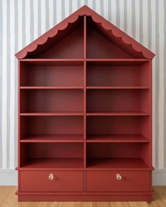Estante Fábula em vermelho, em formato de casinha, com telhado recortado, prateleiras abertas e duas gavetas na base.